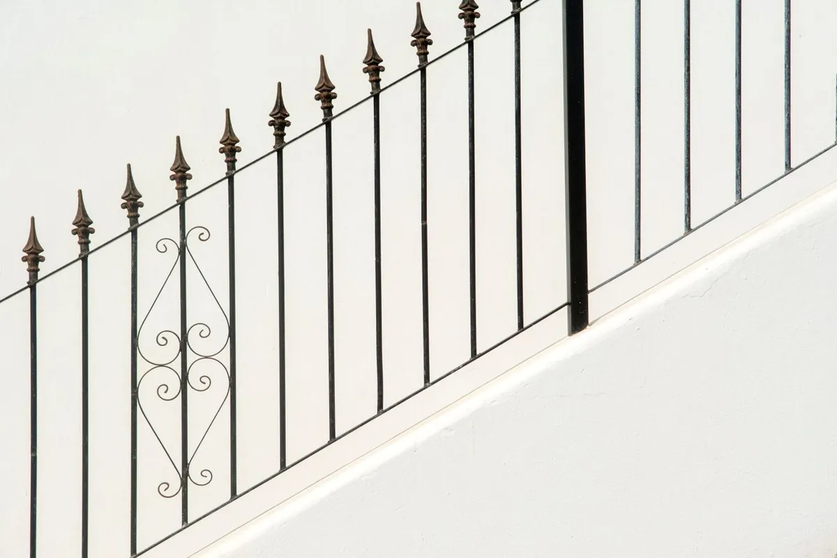 Black iron pickets with spear-point finials set along the top of a white plastered wall that steps up a slope