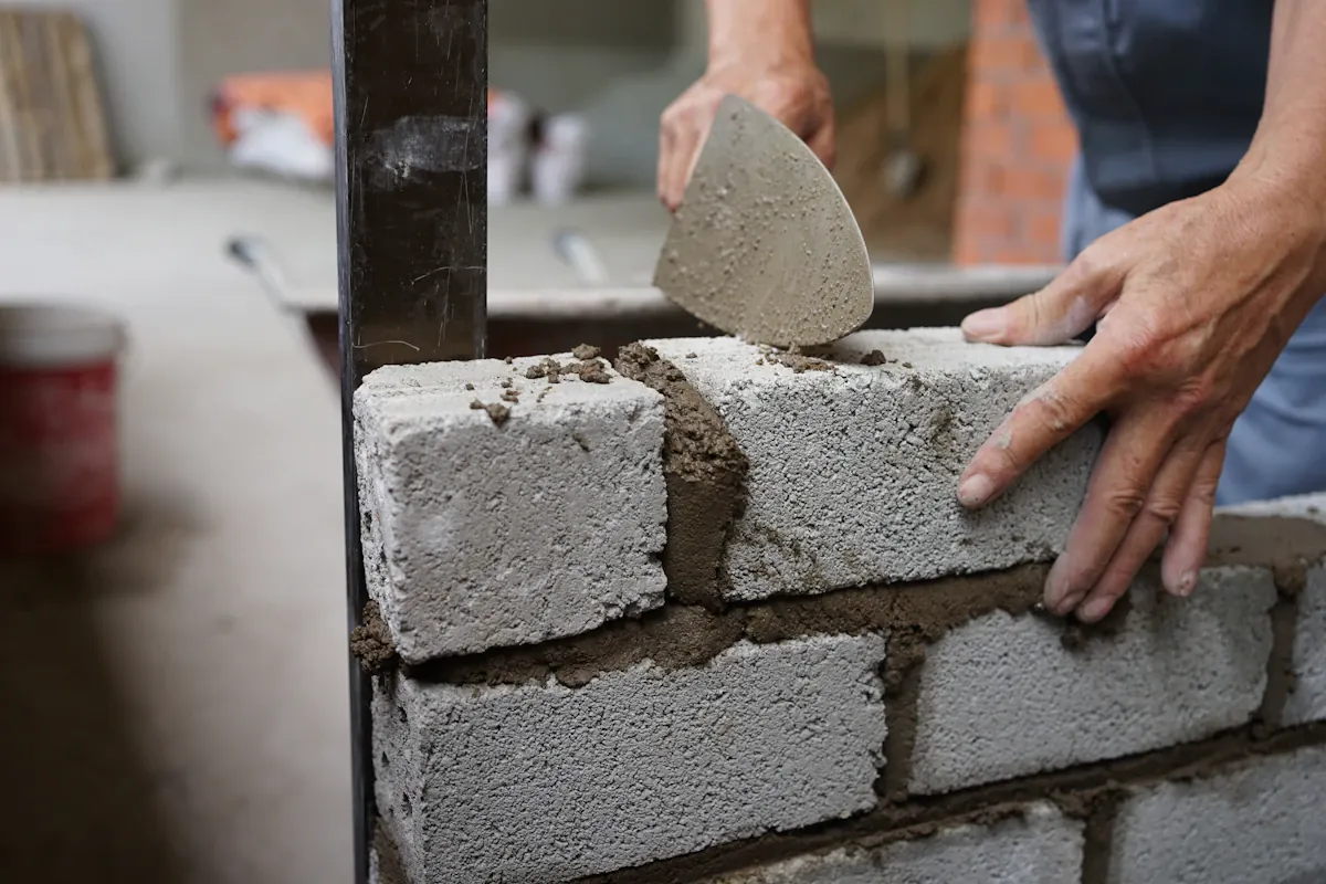 A masonry contractor's hands setting a gray concrete block into fresh mortar with a trowel, the core of Queen Creek masonry work