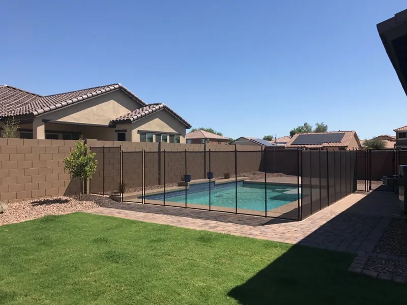 A removable mesh pool fence around a backyard pool inside a tan block wall in Phoenix, a type Queen Creek does not accept as the required pool fence